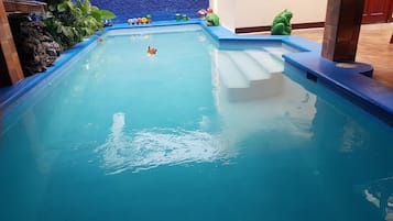 Una piscina con borde de azulejos azules, una repisa de piedra en un lateral y una estatua decorativa de un sapo.