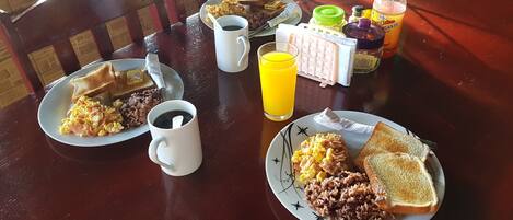 Una mesa de desayuno con platos de huevos, tostadas y arroz, un vaso de jugo de naranja y una taza de café.