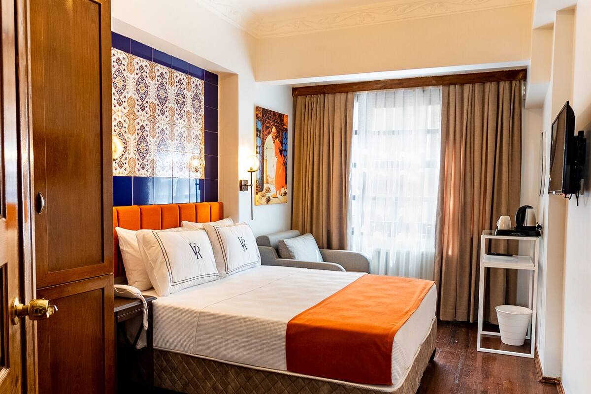 A hotel room with a large bed, a desk, a chair, a TV, and a window with curtains.
