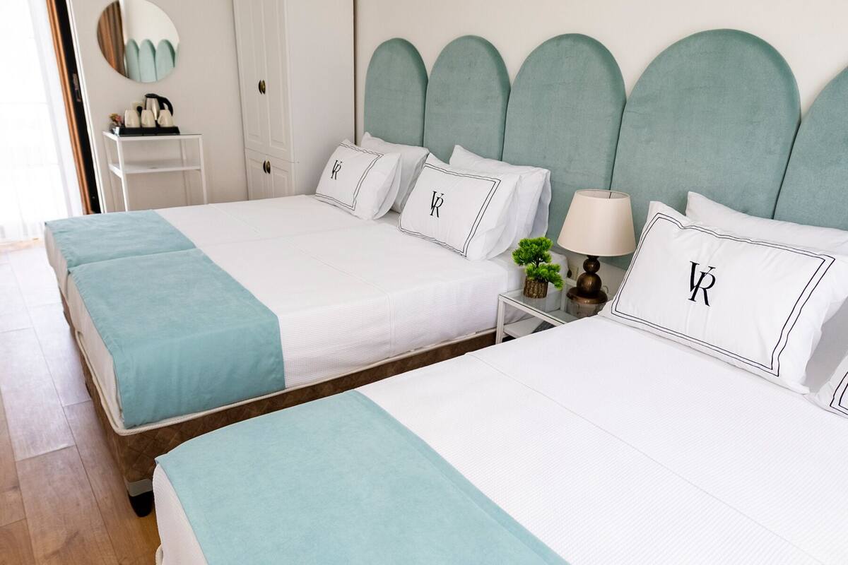 A hotel room with two beds, a wardrobe, a bedside table with a lamp, and a mirror on the wall.