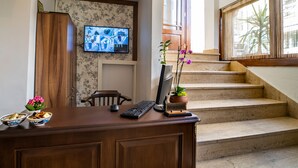 A wooden desk with a computer, a TV mounted on the wall, and a staircase leading to an outdoor area. - Hotel Vera (Istanbul)