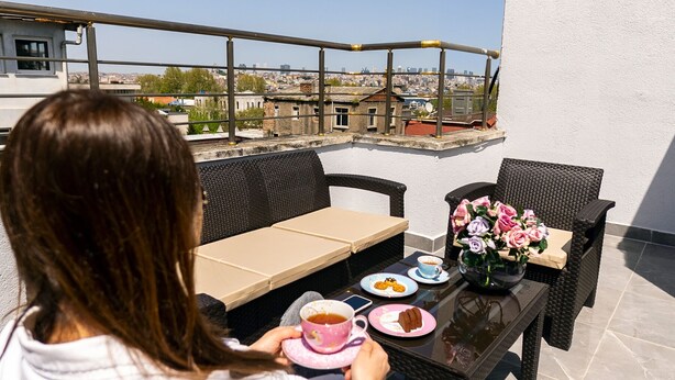 A woman sitting at an outdoor table with a view of a cityscape. The table has a vase with flowers, a plate with food, and a cup. - Hotel Vera (Istanbul)