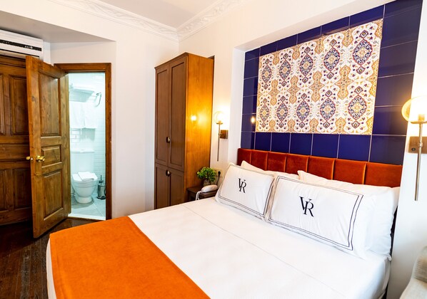 A hotel room with a bed, a wooden wardrobe, a bathroom visible through an open door, and a patterned wall. - Hotel Vera (Istanbul)