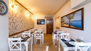 A hotel dining area with white tables and chairs, a wooden floor, and a painting of a beach scene on the wall. - Hotel Vera (Istanbul)