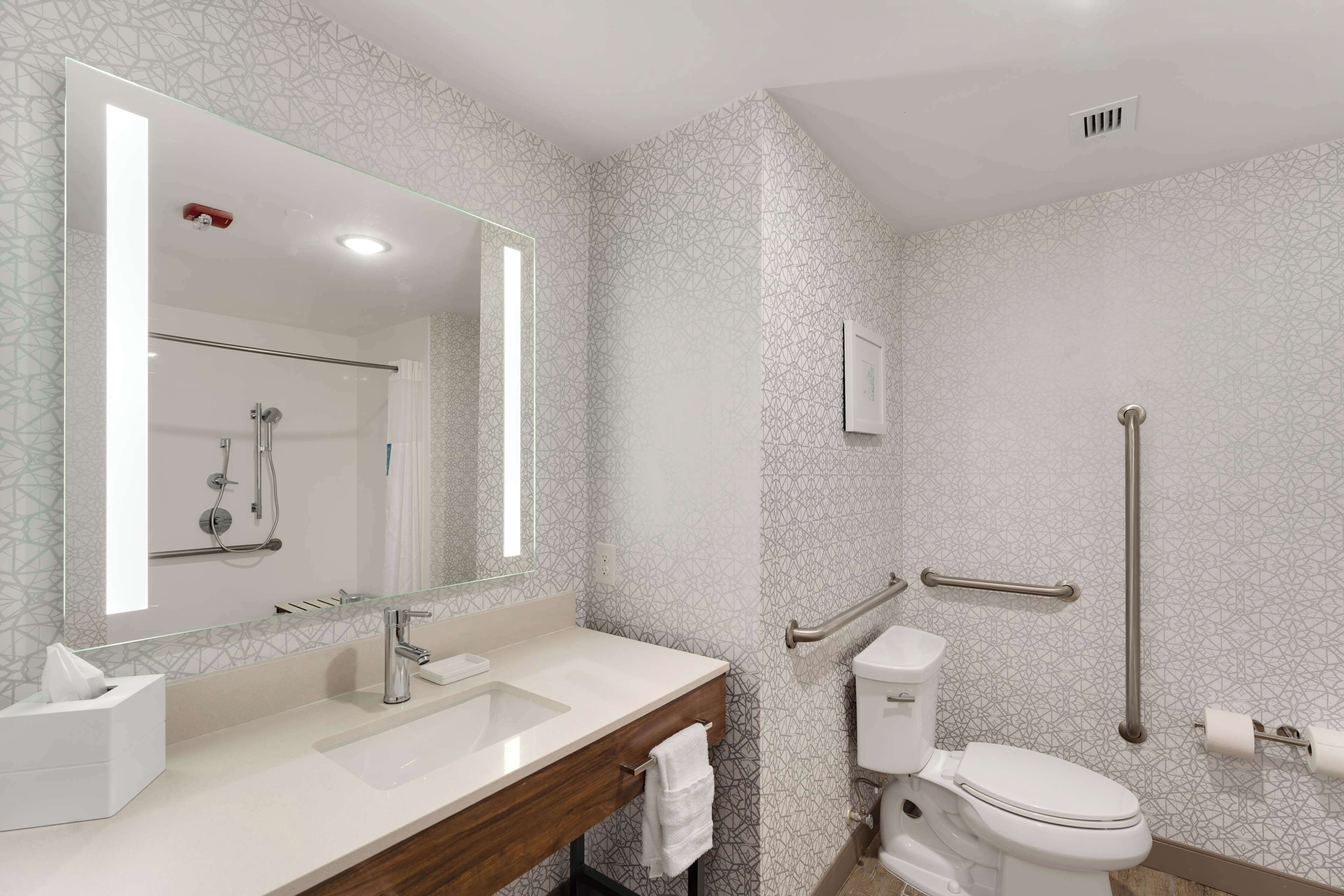 A modern bathroom with a glass shower enclosure, a white sink, a toilet, and a handrail for accessibility.