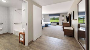 A modern hotel room with a shower, a bed, a desk, and a large window offering a view of the outdoors. - Hampton Inn Milford (Milford)