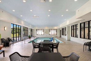A pool area with a table and chairs, large windows, and a sign indicating no lifeguard on duty.
