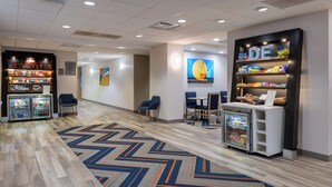 A hotel lobby with a modern design, featuring a patterned carpet, seating areas, a snack bar, and a refrigerator. - Hampton Inn Milford (Milford)