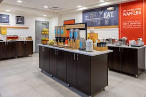 A breakfast bar with coffee machines, a waffle station, and a sign that reads "Happy Breakfast Starts Here".