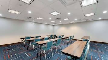 Uma sala de conferências com mesas, cadeiras, luminárias no teto e carpete estampado.