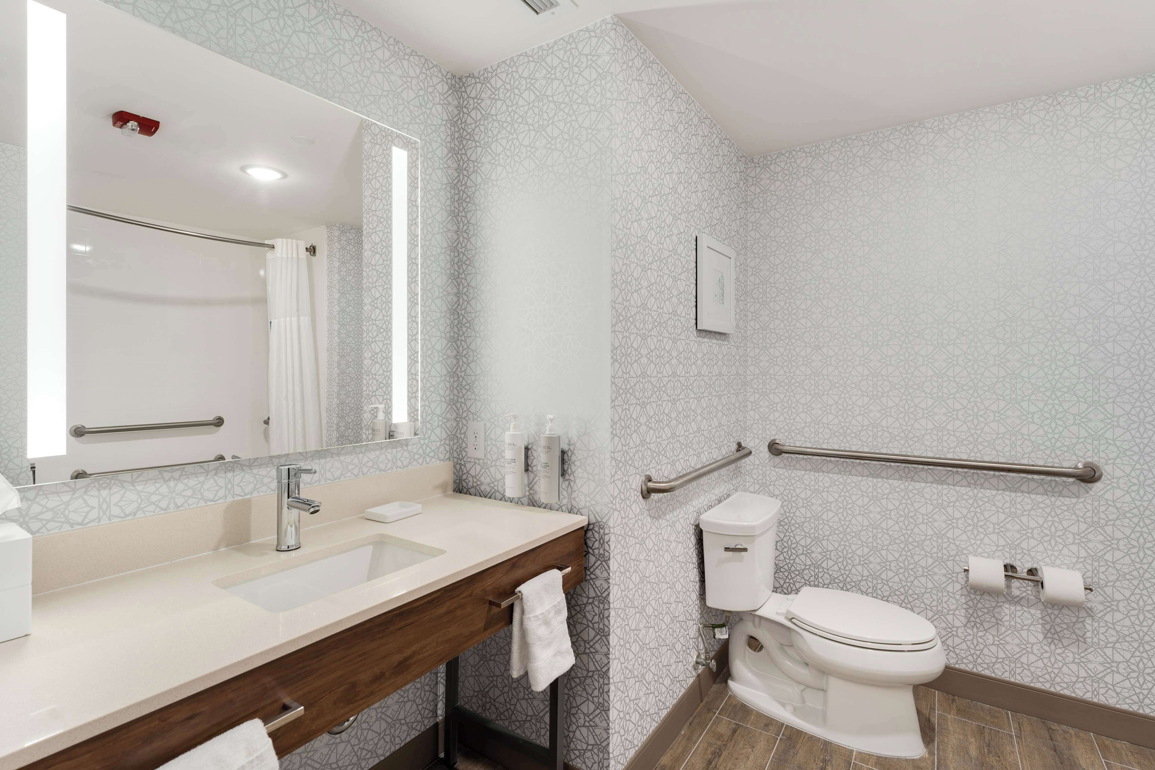 A modern bathroom with a vanity, sink, mirror, toilet, and handrails.