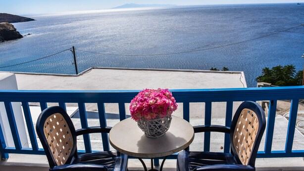 A balcony with a table and chairs, overlooking a coastal view. - Anemos Studios (Andros)