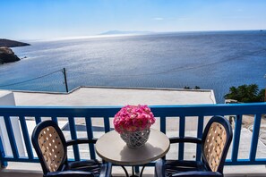 A balcony with a table and chairs, overlooking a coastal view. - Anemos Studios (Andros)