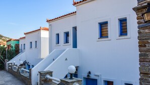 A row of white buildings with blue shutters and a stone staircase leading to the entrance. - Anemos Studios (Andros)