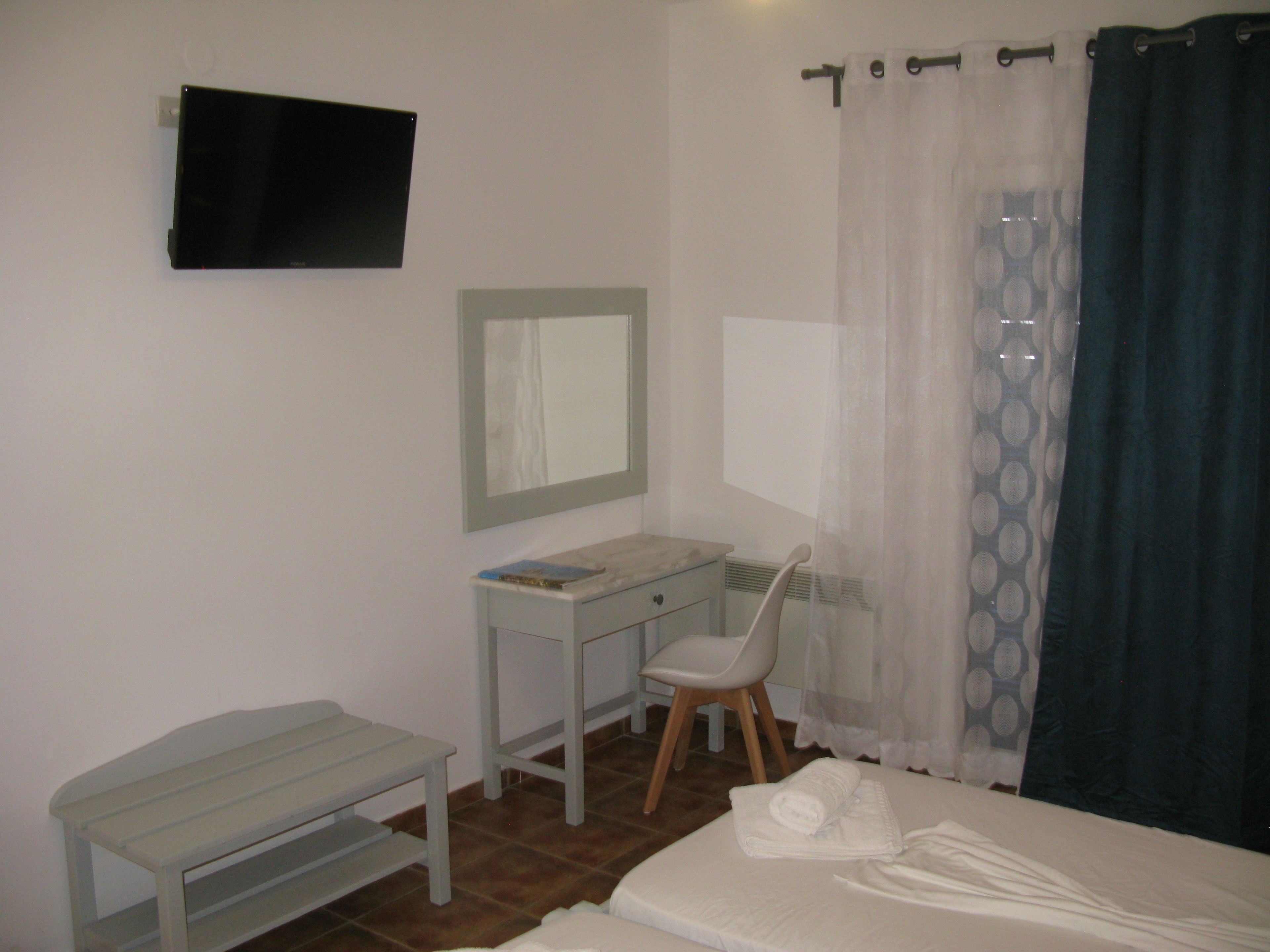 A bedroom with a bed, a desk, a chair, a TV, and a window with curtains.