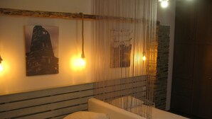 A bed with white linens, a headboard with horizontal lines, and a wall with a framed picture and two wall-mounted lights. - Anemos Studios (Andros)