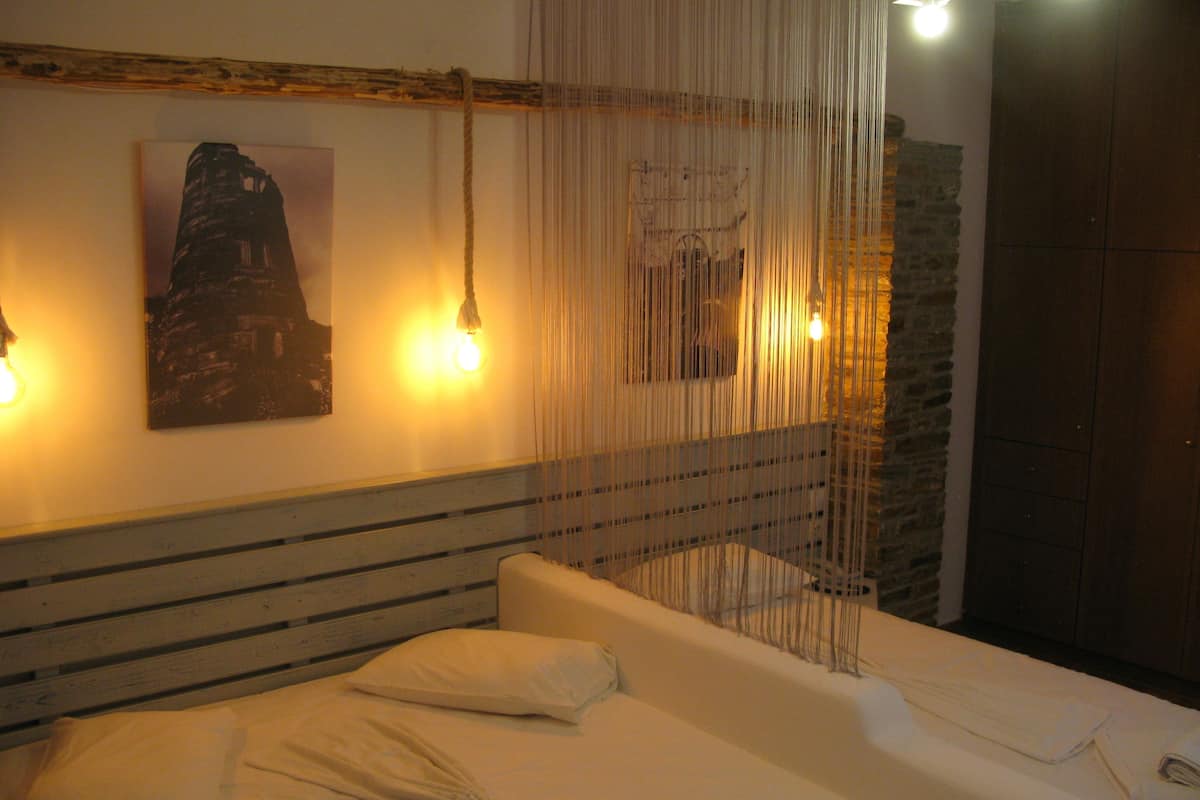 A bed with white linens, a headboard with horizontal lines, and a wall with a framed picture and two wall-mounted lights.