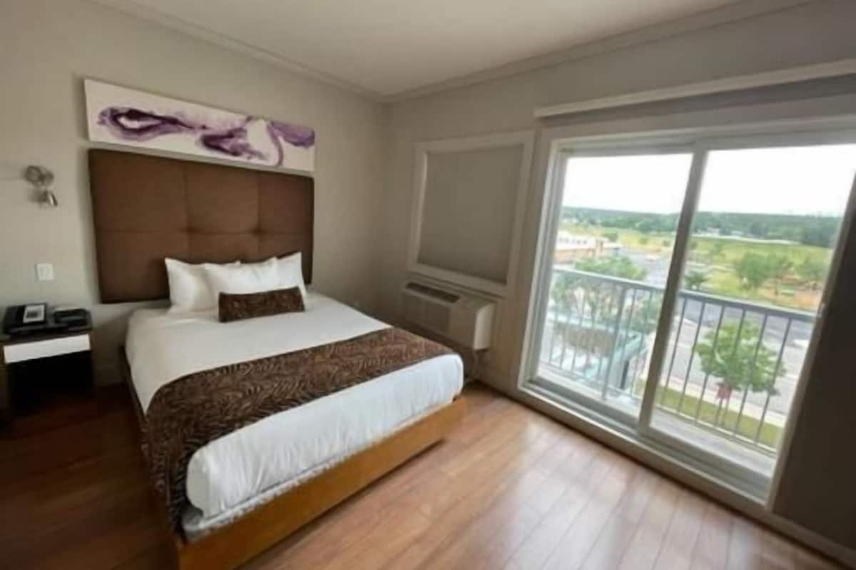 Un dormitorio con una cama grande, cabecera, mesita de noche y una ventana con vistas, además de una lámpara en el techo.