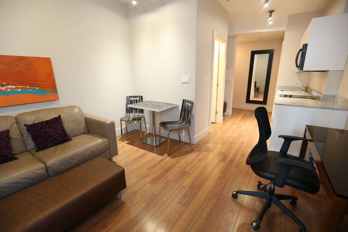 Una sala de estar moderna con sofá, una mesa de comedor con sillas y una zona de cocina con encimera y fregadero.