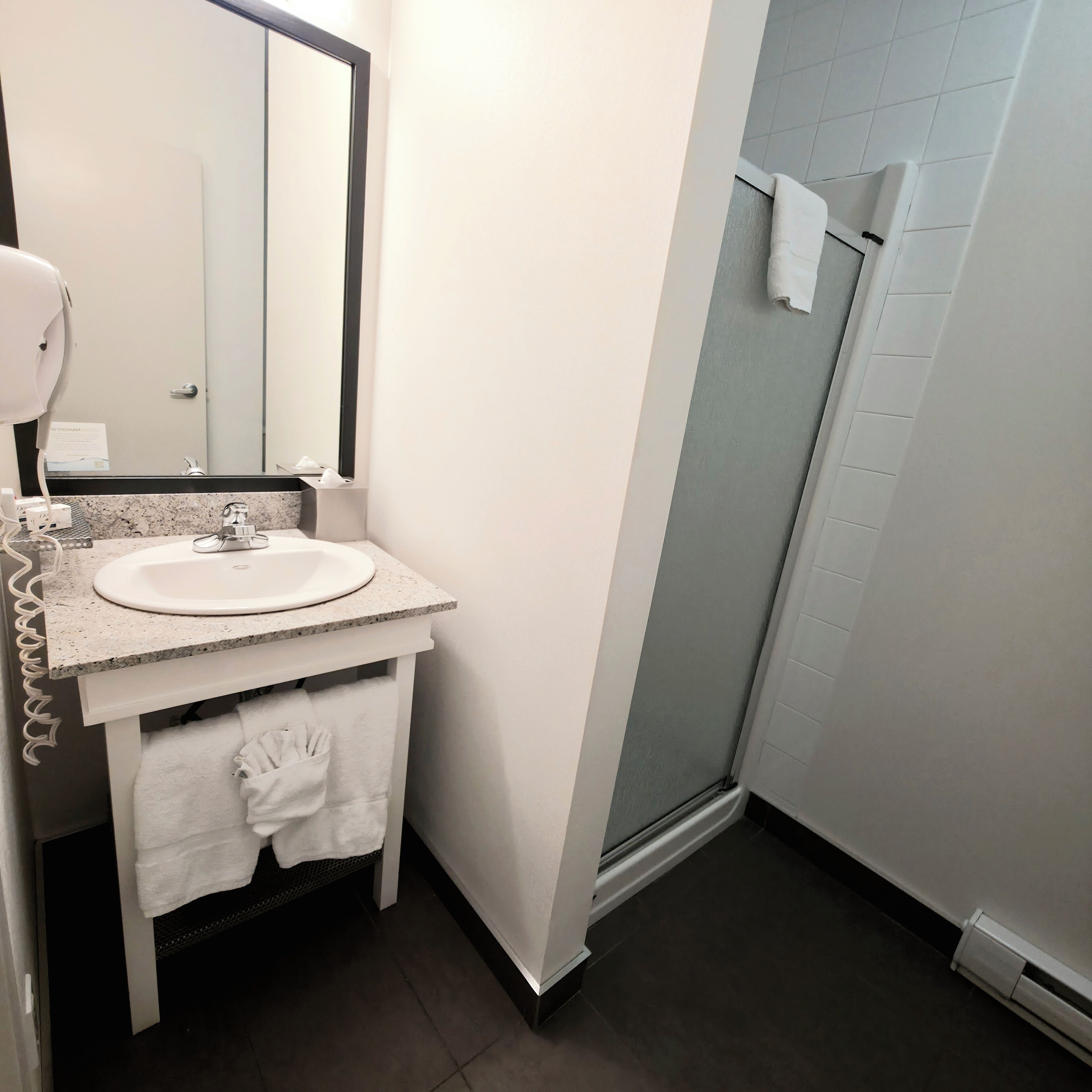 A bathroom with a sink, mirror, towel rack, and a shower area.