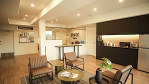 Een moderne hotel lobby met lederen zitplaatsen, een centrale tafel en een keuken in de achtergrond.