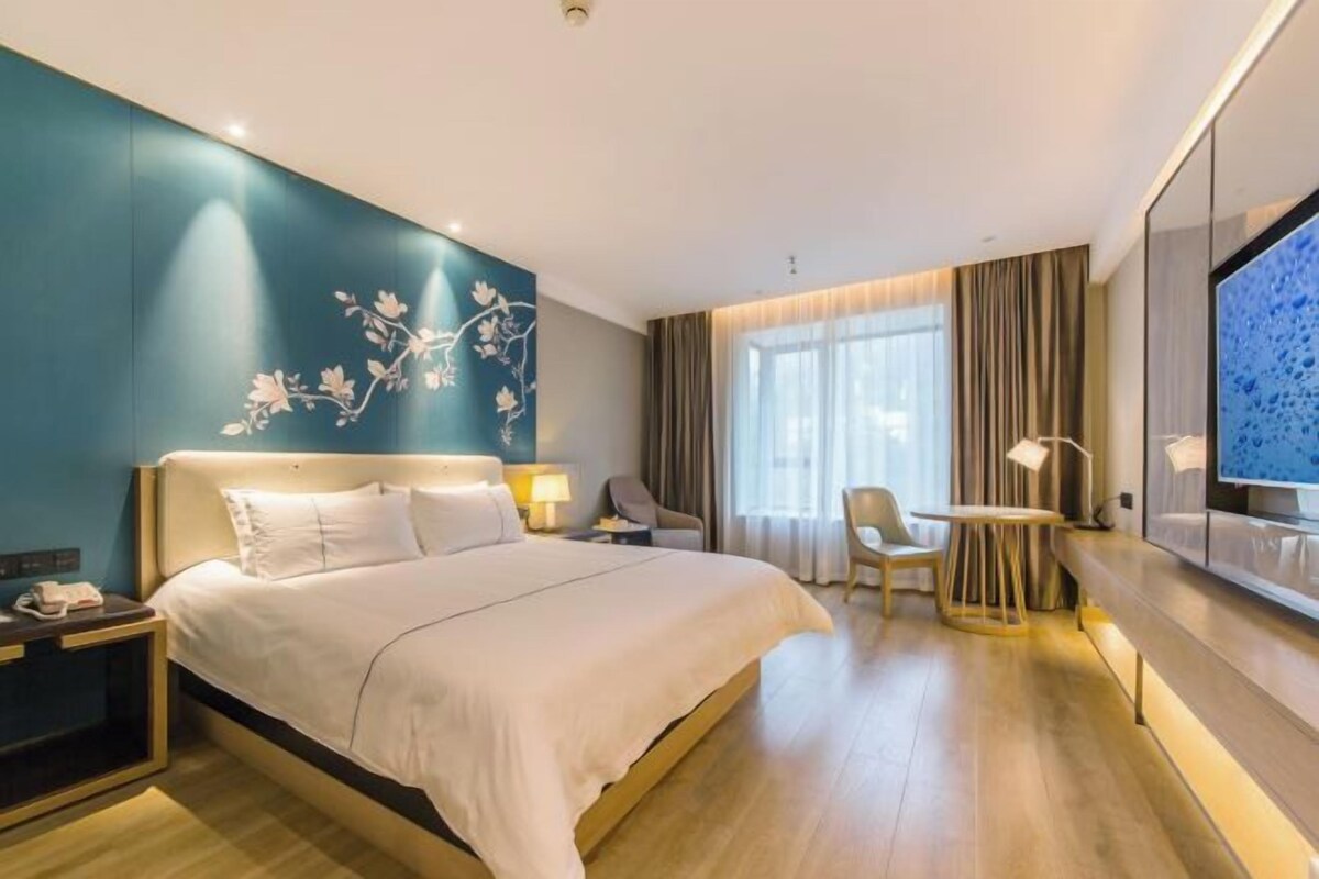 A hotel room with a large bed, a desk, a chair, and a TV.