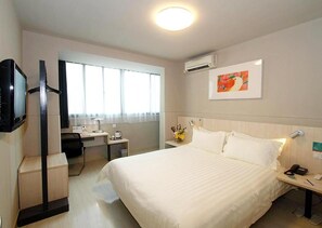 A hotel room with a large bed, a desk with a chair, a TV, and a window with curtains.