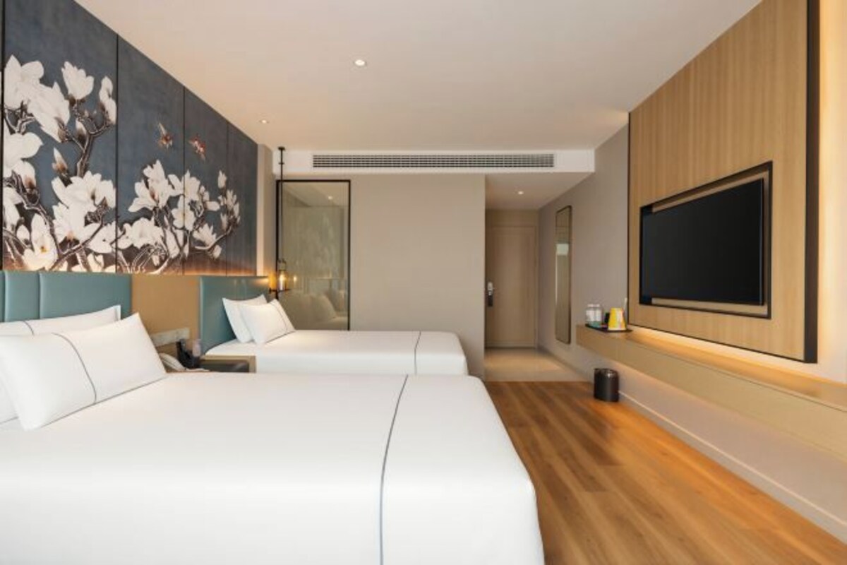 Habitación de hotel con dos camas, un televisor grande montado en la pared y un cuadro.