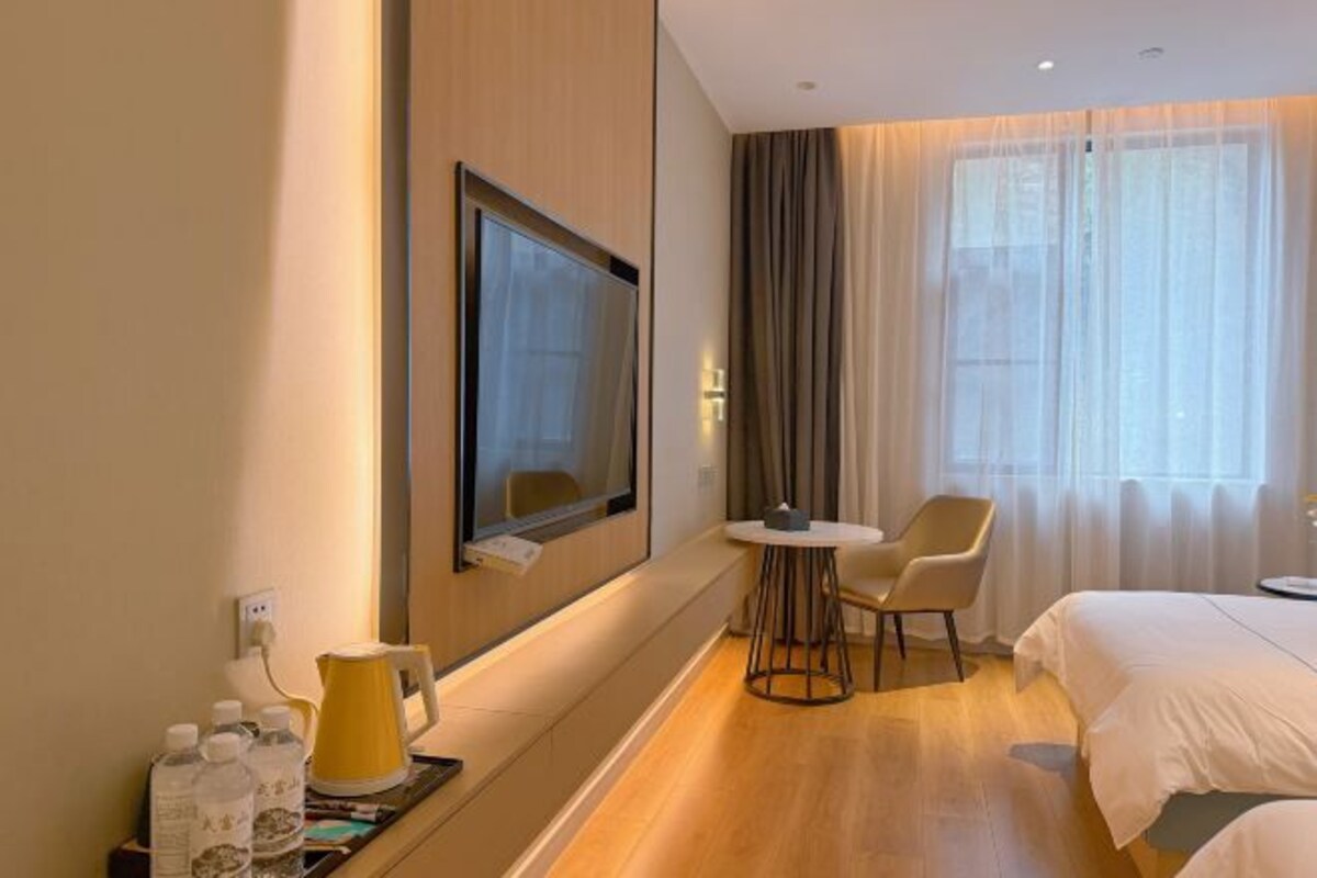Habitación de hotel con cama, televisor montado en la pared, una mesita con sillas y ventana con cortinas.