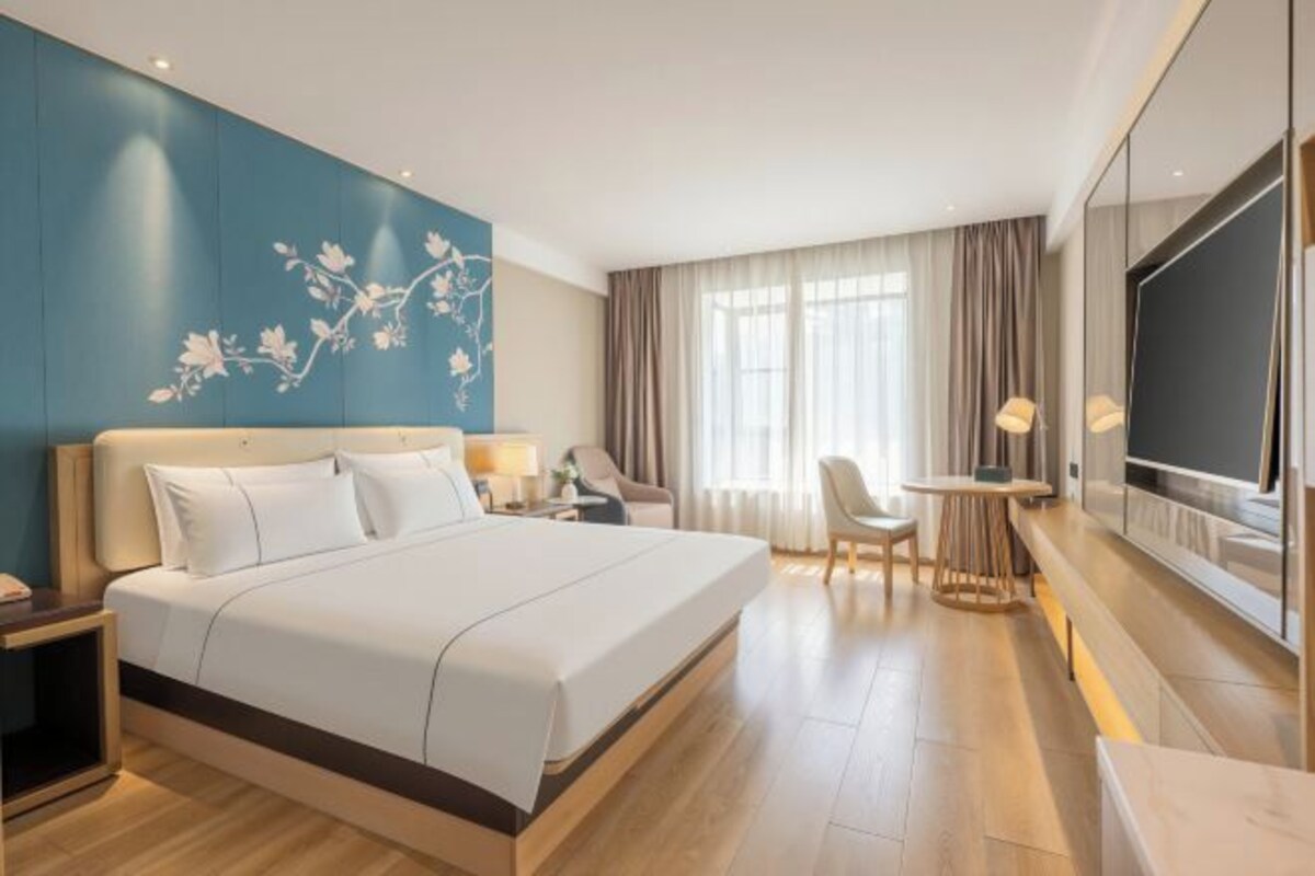 Habitación de hotel con una cama grande, un escritorio, una silla, un televisor y una pared decorada con un diseño floral.
