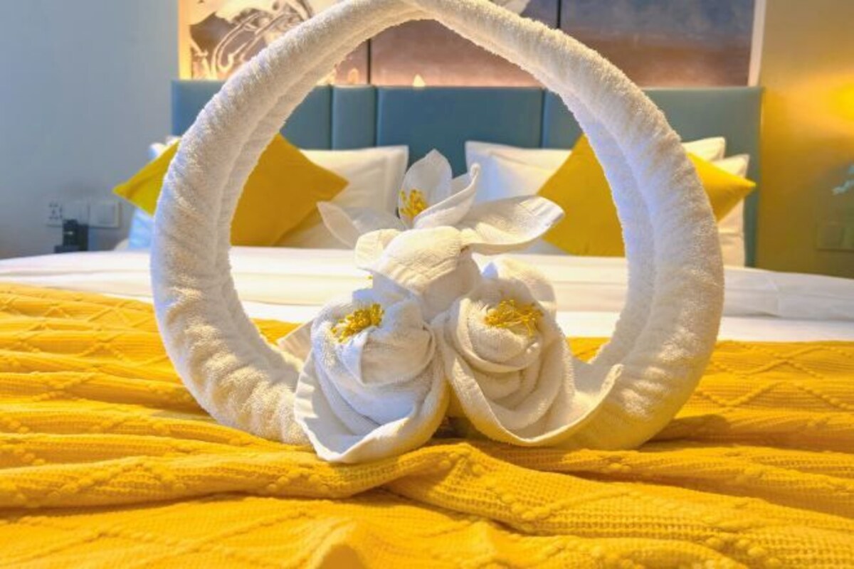 Una cama con un tozaleta blanca y dos toallas blancas formando flores, sobre un edredón amarillo.