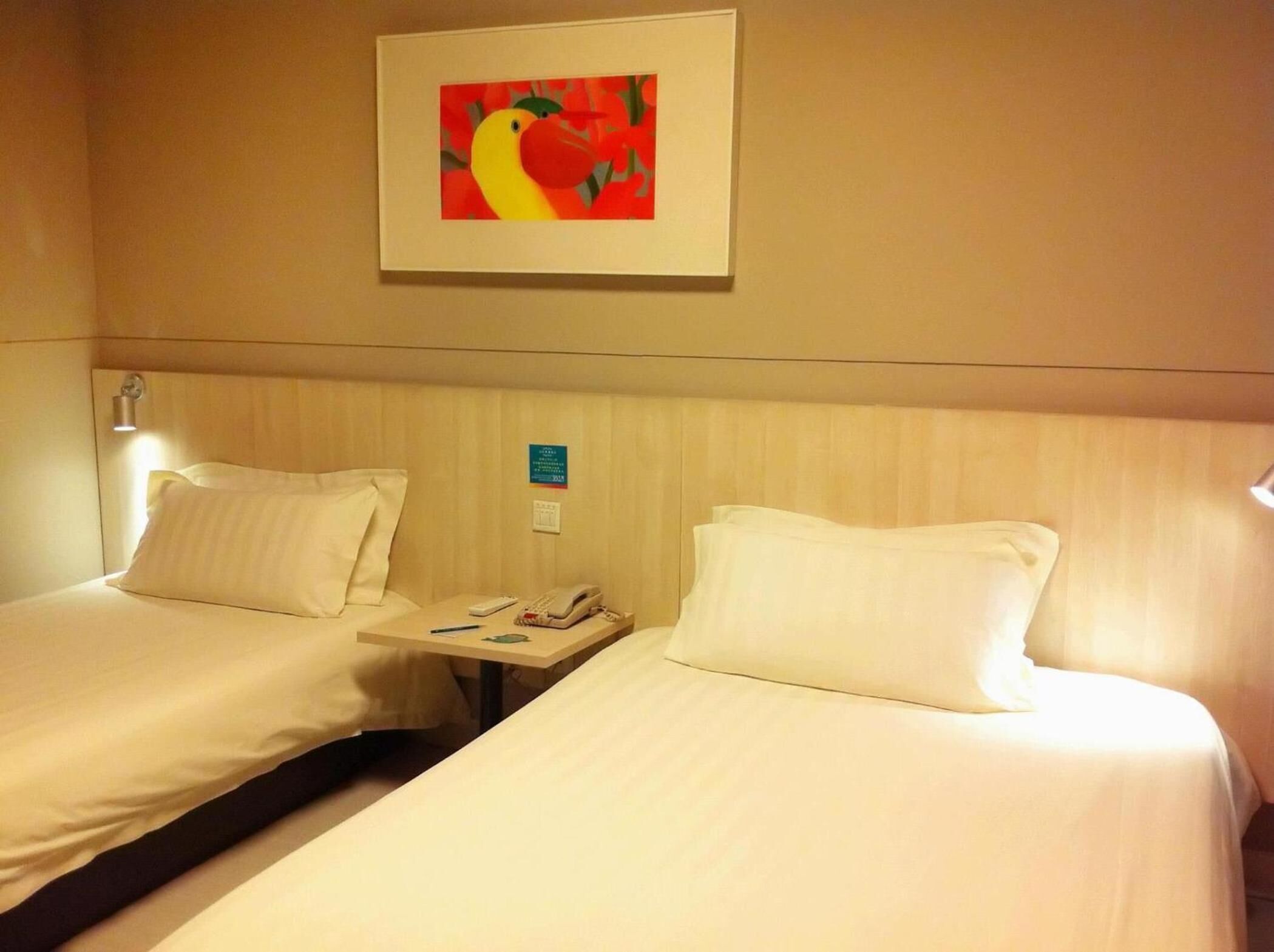Een hotelkamer met twee bedden, een nachtkastje, een telefoon en een schilderij aan de muur.