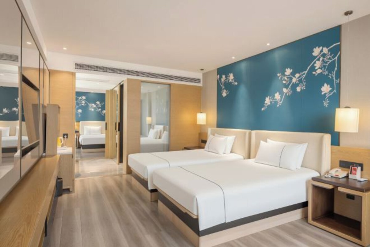 Habitación de hotel con dos camas, un espejo, una mesita de noche y una pared con motivos florales.