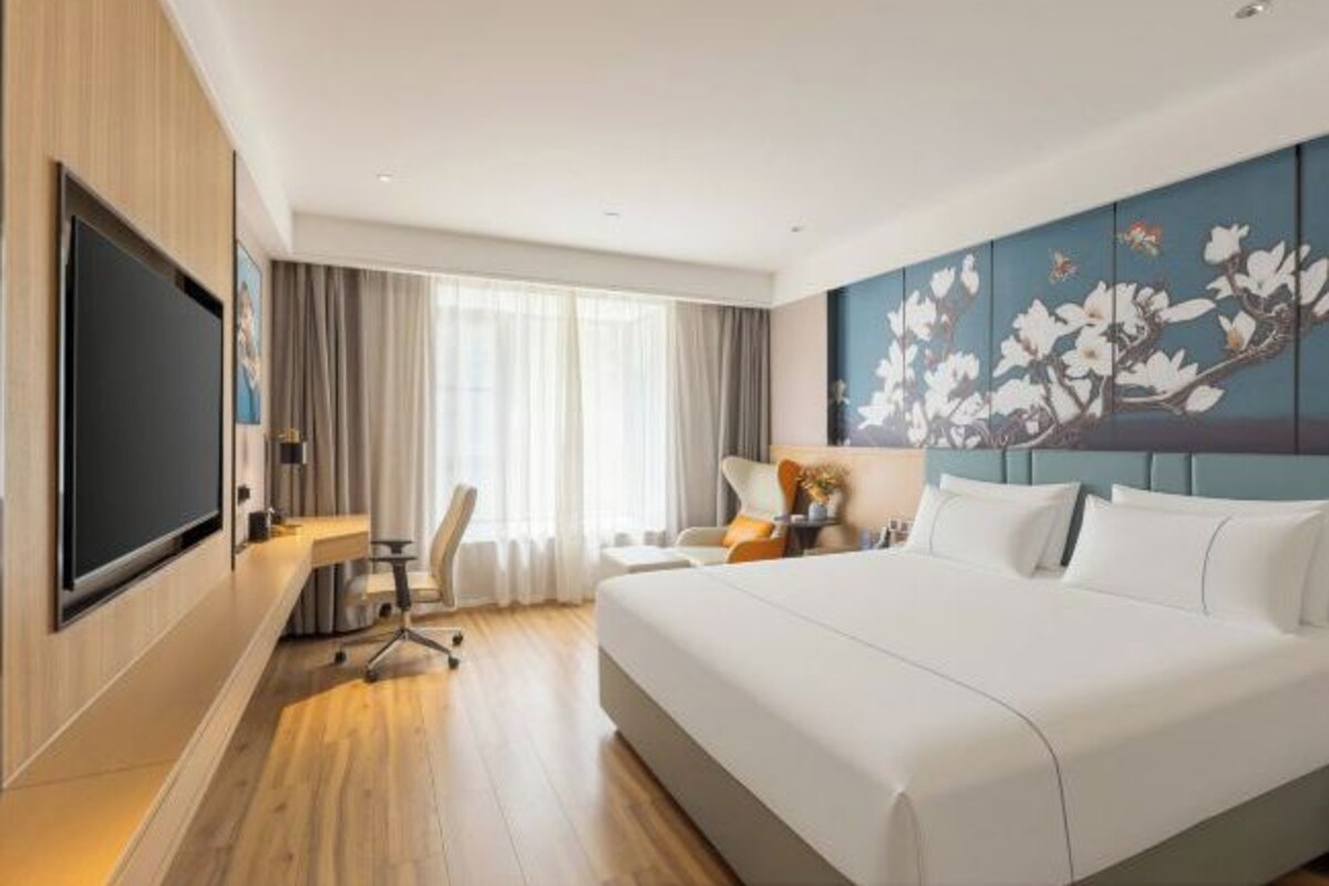 Habitación de hotel con una cama grande, un escritorio con silla, televisor de pantalla plana y un ventanal con cortinas.