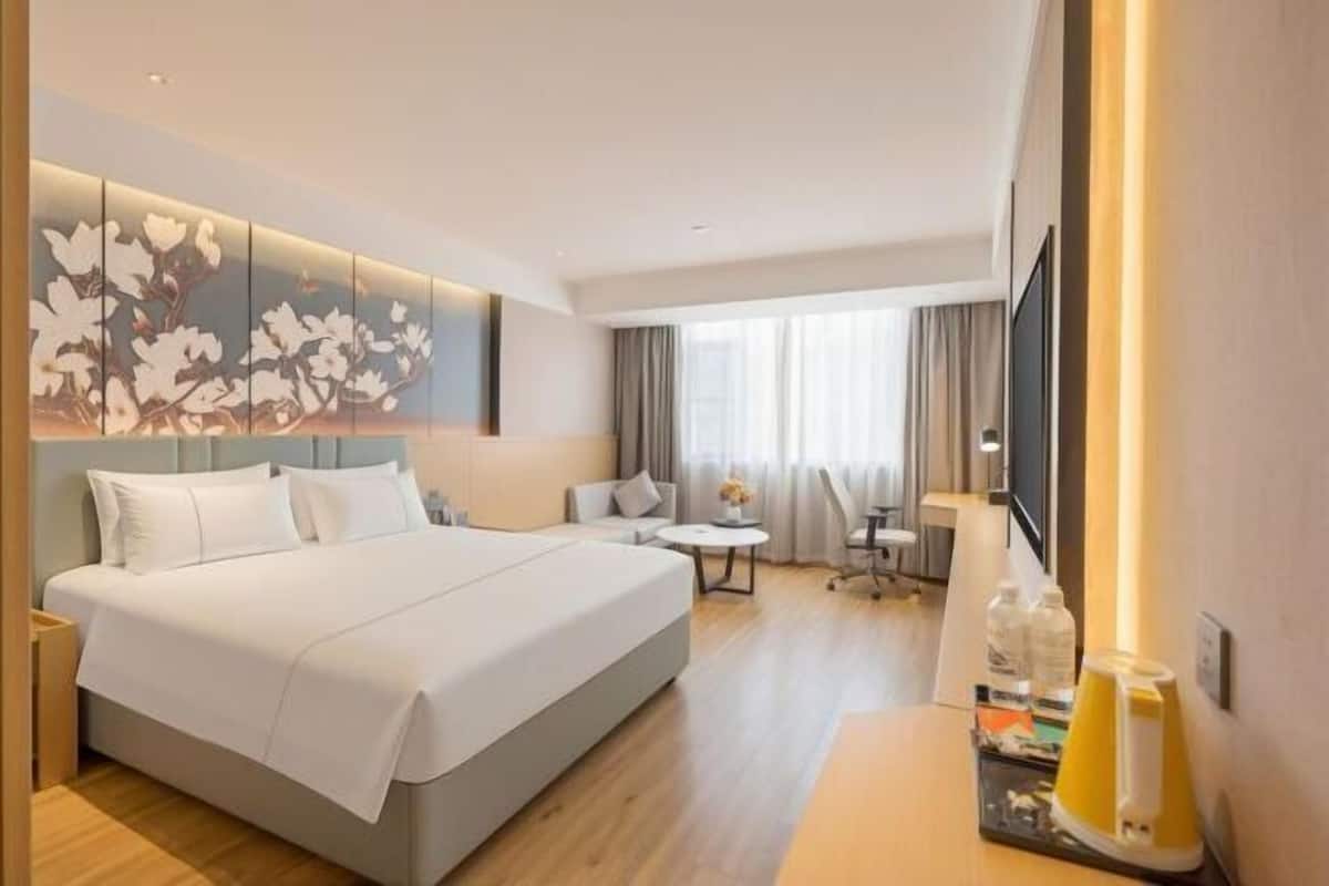 A hotel room with a large bed, a desk, a chair, a TV, and a wall-mounted artwork.