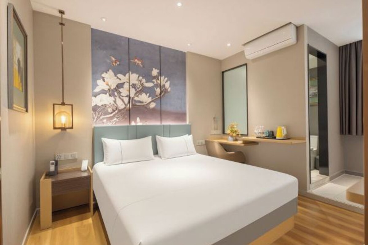 Una habitación de hotel moderna con una cama grande, un escritorio, una silla, un cuadro y un espejo.