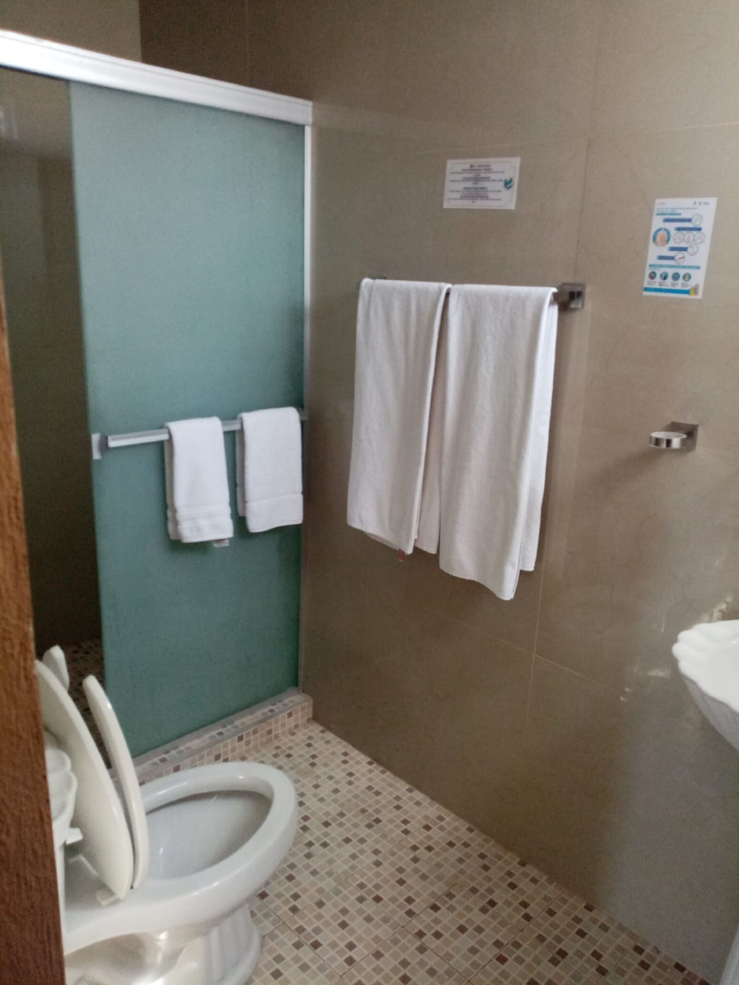 Un baño con inodoro, cabina de ducha y lavabo. Hay dos toallas colgadas en la pared.