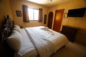 A hotel room with a large bed, a wooden dresser, a television mounted on the wall, and a window with curtains. - Hotel La Casona Real (Cozumel)