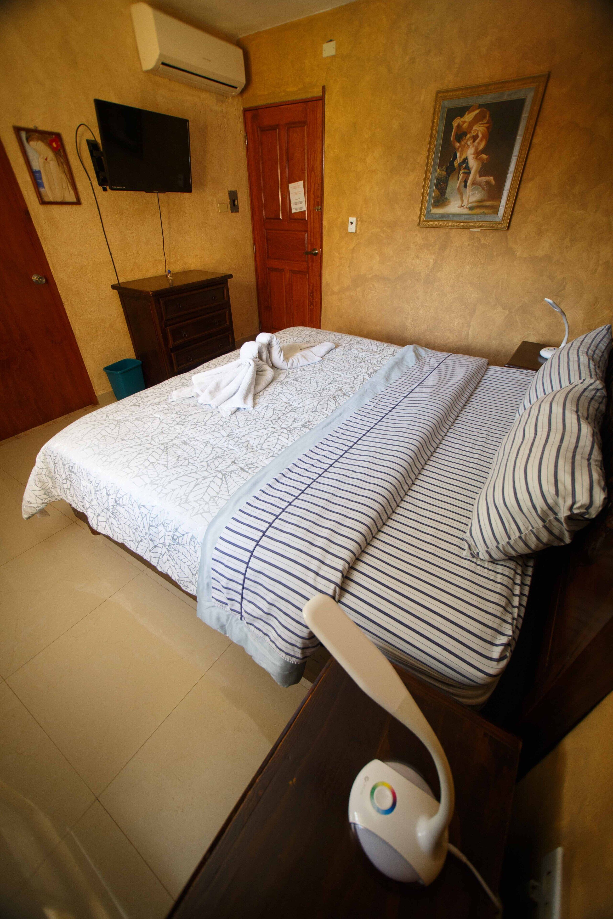 A neatly made bed with striped bedding, a television mounted on the wall, and a painting above the bed.