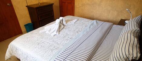 A neatly made bed with striped bedding, a television mounted on the wall, and a painting above the bed.
