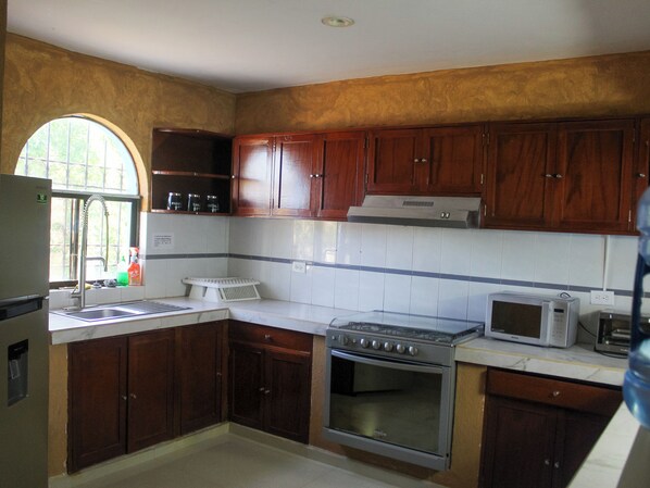 Una cocina con armarios de madera, una estufa de acero inoxidable, un microondas y un lavamanos con ventana superior.