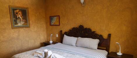Una cama bien tendida con un edredón blanco y azul a rayas, un cabecero de madera y un ventilador de techo.