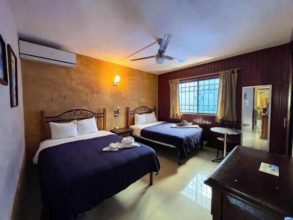 A hotel room with two beds, a ceiling fan, a window with curtains, a small table, and a mirror. - Hotel La Casona Real (Cozumel)