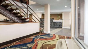 A modern hotel lobby with a staircase, a reception desk, and a patterned carpet.