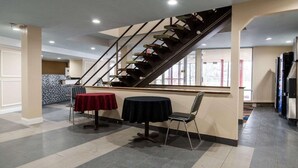 A spacious indoor area with a central staircase, two round tables with chairs, and a kitchen area in the background.