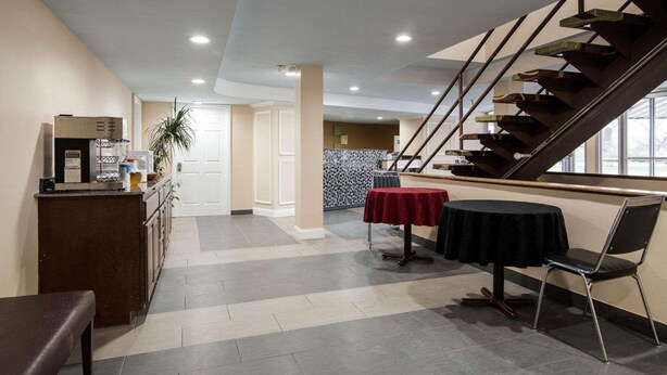 A hotel lobby with a staircase, a reception desk, and a dining area with tables and chairs.