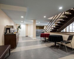 Un vestíbulo de hotel con una escalera, un mostrador de recepción y una zona de comedor con mesas y sillas.