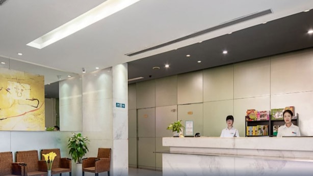 A reception area with a marble reception desk, two receptionists, and a seating area with wicker chairs. - Jinjiang Inn Shenzhen Airport (Shenzhen)