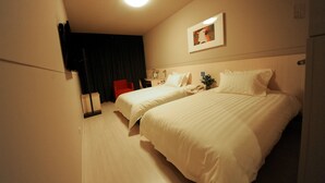 A hotel room with two beds, a desk, a chair, a nightstand, and a ceiling light.