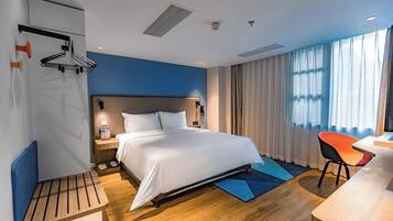 A modern hotel room with a large bed, bedside table, and a desk with a chair.